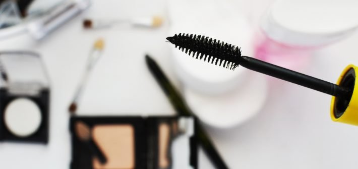Black eyelash mascara wand infront of blurred compact mirror