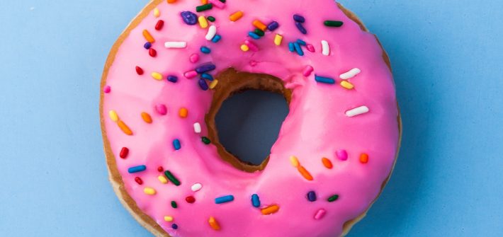 Valentine's Day donut with pink glaze and multicolored sprinkles on blue background
