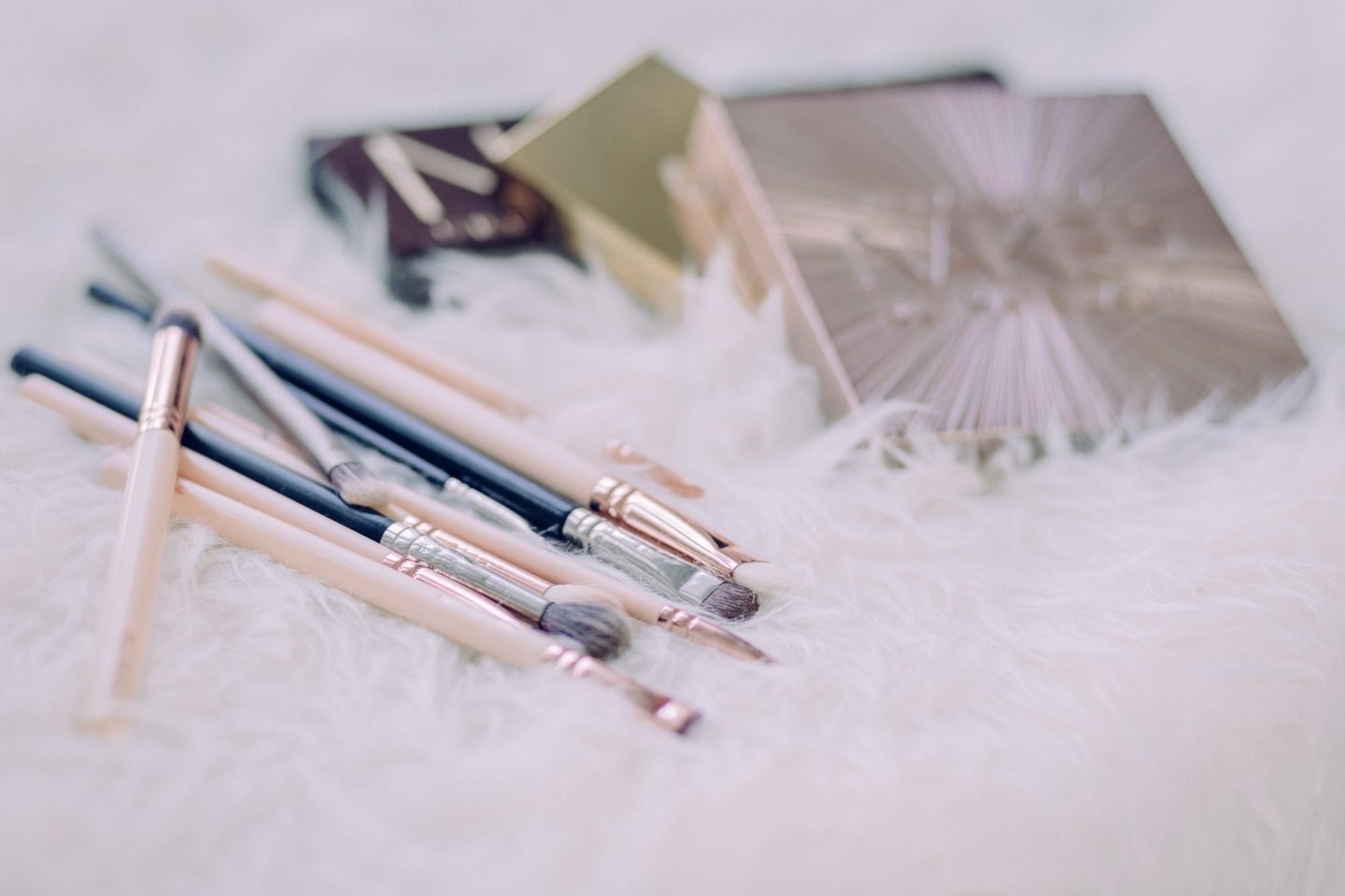 assorted makeup brushes and beauty boxes on white fur