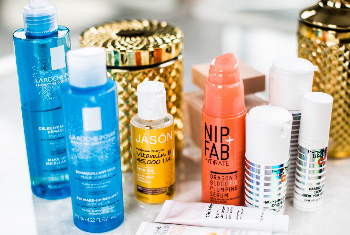 Skincare bottles lined up on white table next to mirror. How to organize your skincare