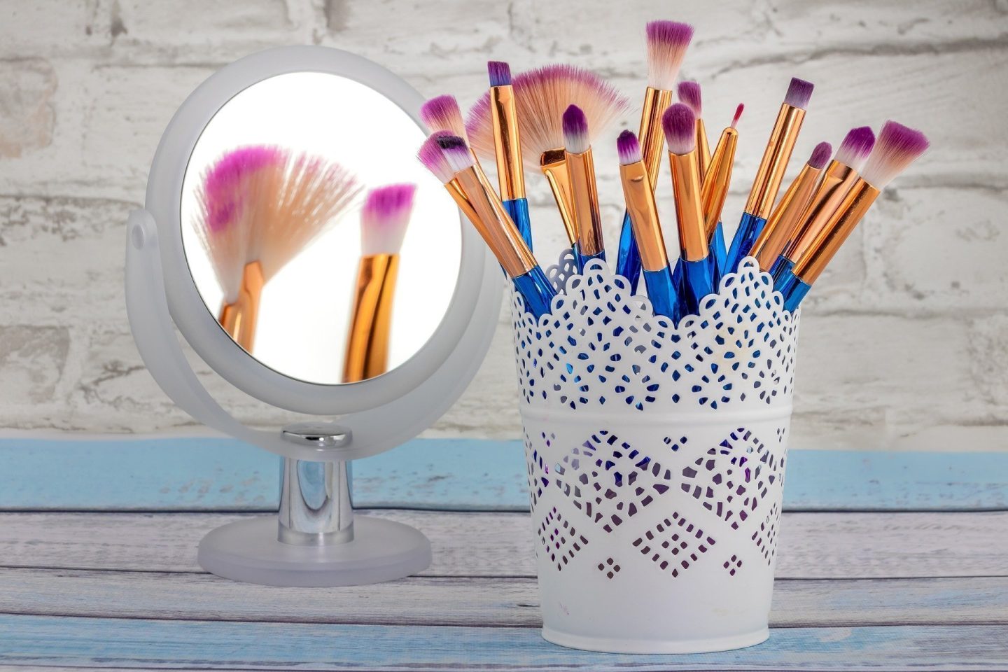 blue makeup brushes in a white container next to round mirror 